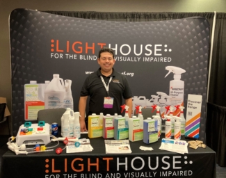 Alex Flores stands behind a table of cleaning products, manufactured at LightHouse Sirkin Center, at the 2023 NIB Expo