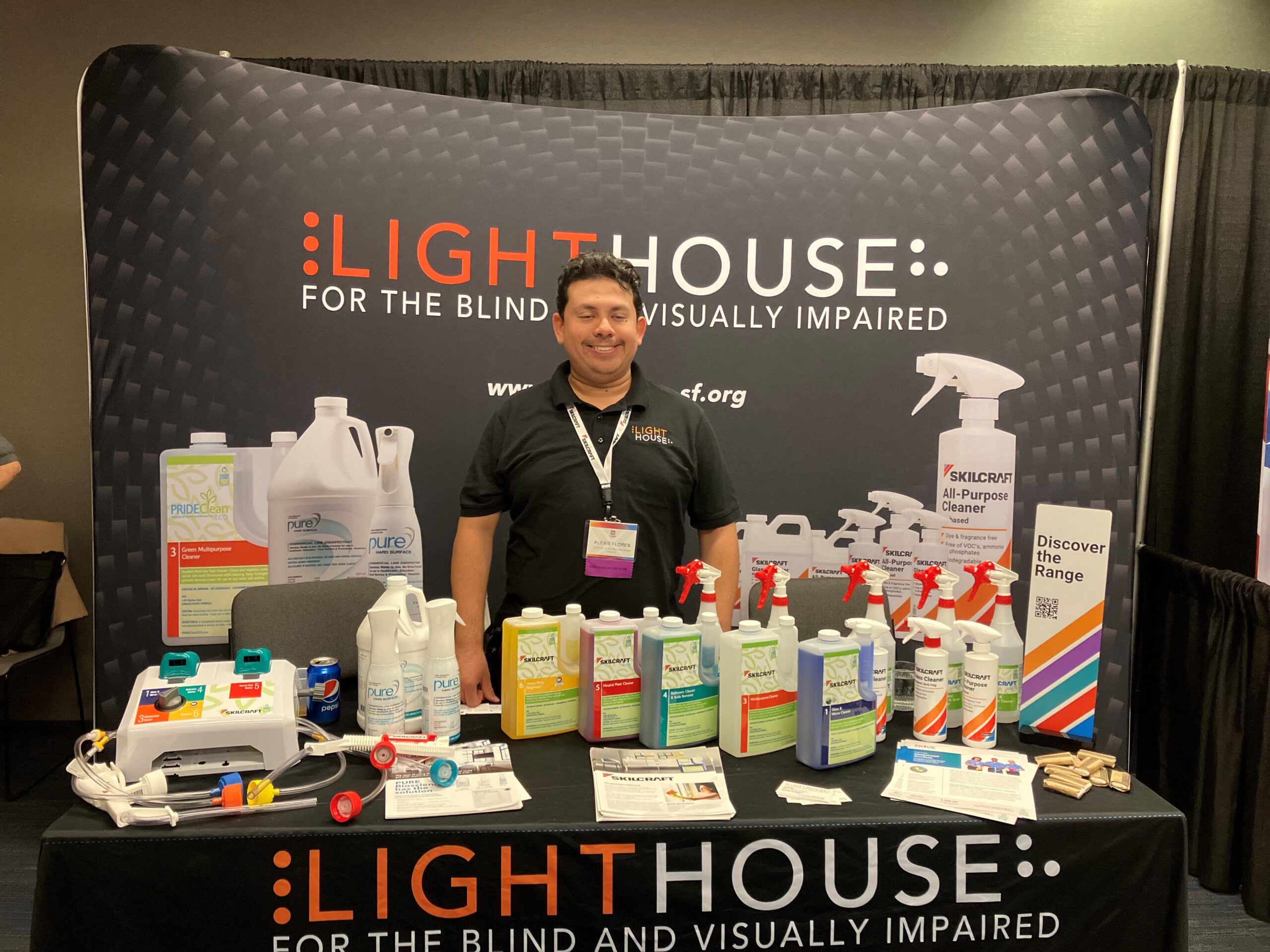 Alex Flores stands behind a table of cleaning products, manufactured at LightHouse Sirkin Center, at the 2023 NIB Expo