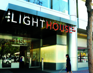 A blind person with walking with their long white cane entering LightHouse headquarters.