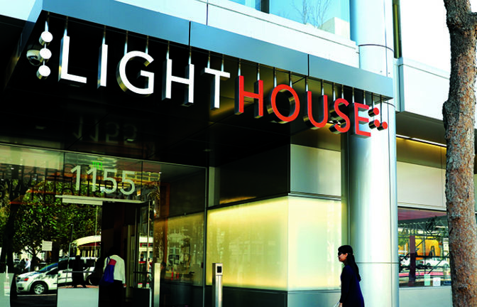 A blind person with walking with their long white cane entering LightHouse headquarters.
