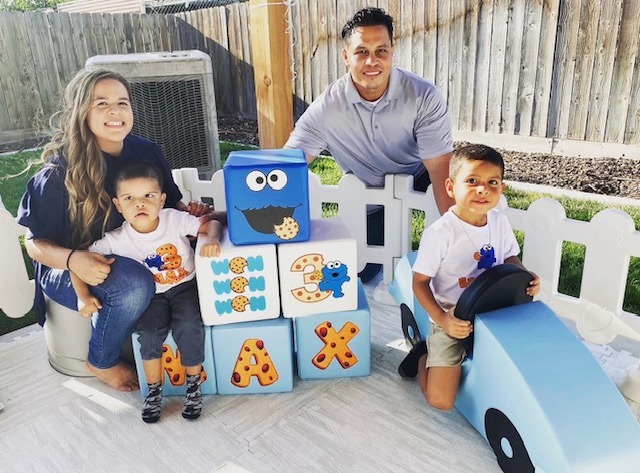 Mom, Dad, Sibling and Little Learner Max pose around Cookie Monster themed party decorations and blocks that say “MAX”