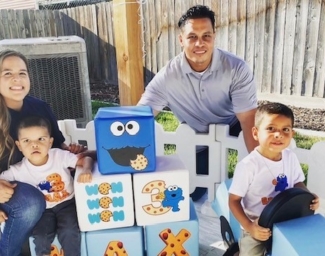 Mom, Dad, Sibling and Little Learner Max pose around Cookie Monster themed party decorations and blocks that say “MAX”