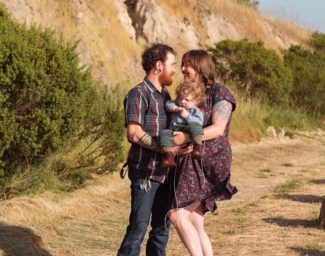 Mom and Dad hold their Little Learner, Ottis, as they pose for a family portrait in a park
