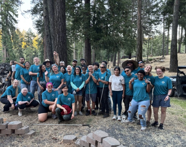2025 EHC Summer Camp staff pose together around the campfire in their matching teal-colored staff t-shirts