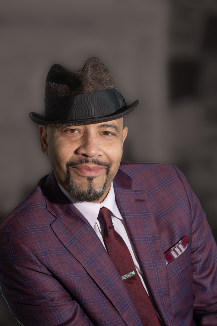 William Rhodes wearing a burgundy and purple plaid suit and a hat.