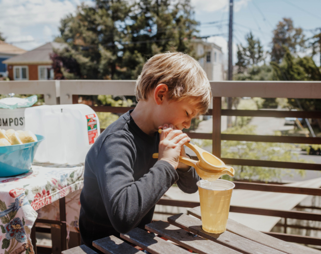 A little boy makes lemonade by squeezing a lemon into a cup filled with water and sugar
