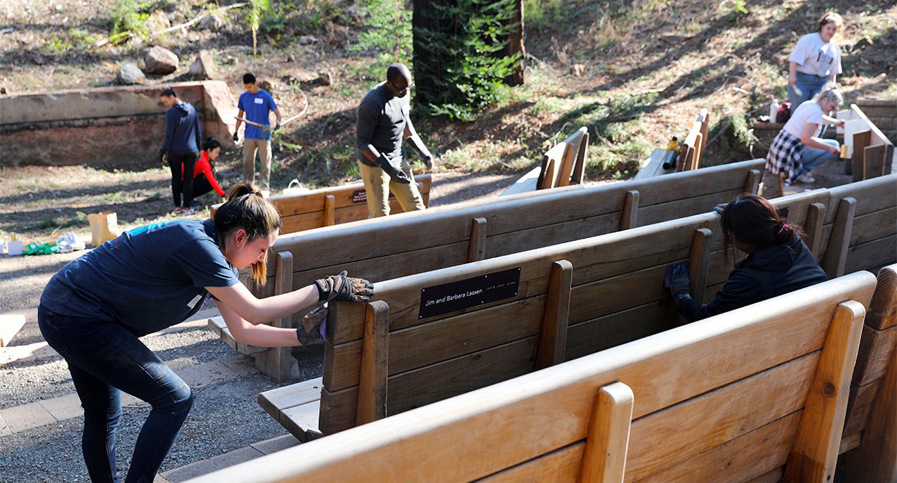 Volunteers sand the Redwood Grove benches at EHC in preparation for treating the wood.