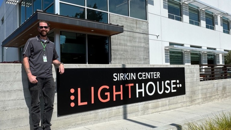 Taylor stands beside the LightHouse Sirkin Center sign at our manufacturing facility in Alameda