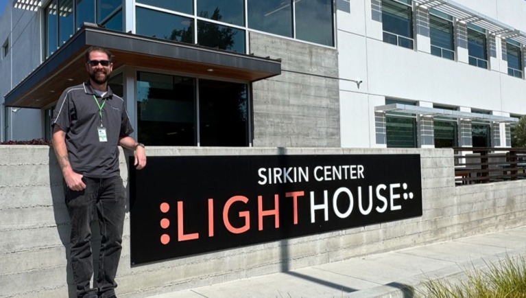 Taylor stands beside the LightHouse Sirkin Center sign at our manufacturing facility in Alameda