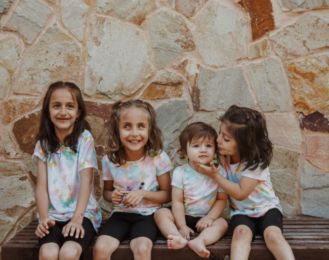 Four little campers in matching tie-dyed t-shirts sit on a bench in the EHC dining hall. Photo Credit: Emmalaine Berry Photography
