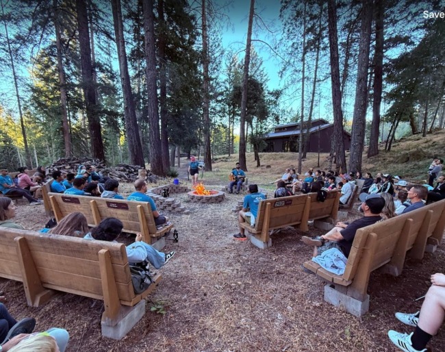 A large group of campers are gathered around the campfire