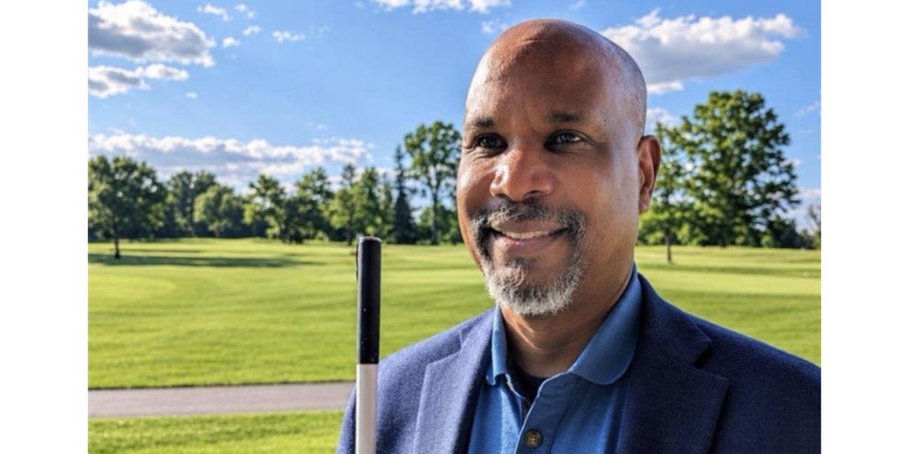 Anil Lewis, incoming LightHouse CEO, smiling outdoors in a navy blazer, holding a white cane.