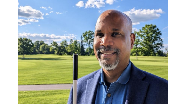Anil Lewis, incoming LightHouse CEO, smiling outdoors in a navy blazer, holding a white cane.