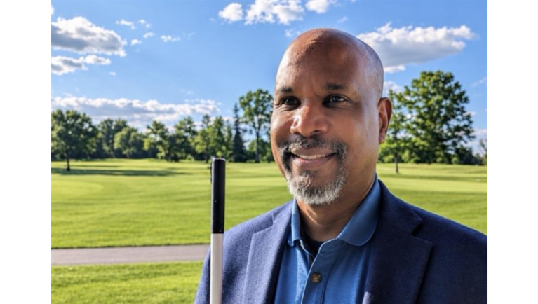 Anil Lewis, incoming LightHouse CEO, smiling outdoors in a navy blazer, holding a white cane.