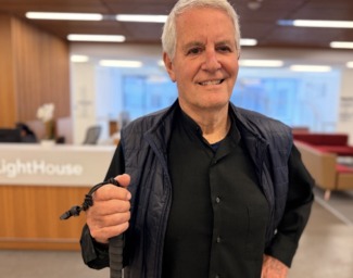 Dr. Harvey Brody poses holding his white cane in front of the LightHouse reception desk