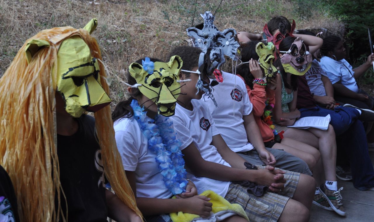 Cast of the Teen Session production of The Lion King sit in a row wearing colorful paper masks