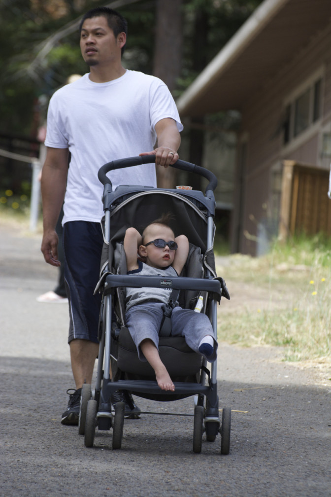 Baby, resembling a celebrity in shades and tank-top, reclines in stroller