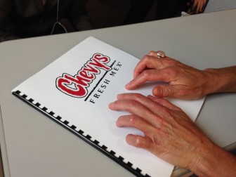 Hands reading a LightHouse produced braille Chevys menu
