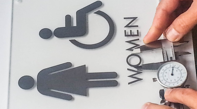 person measuring restroom signage