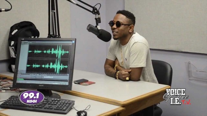 Kendrick Lamar sits at a microphone, wearing sunglasses