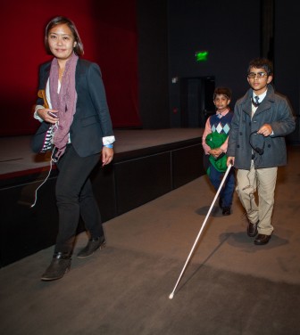 a well-dressed boy with a white cane walks with his friends and family