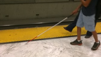 A LightHouse student uses a white cane to detect yellow detectable warning strip on a Muni platform