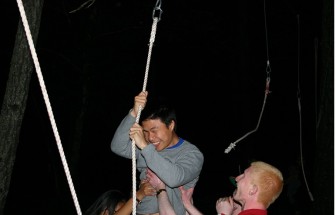 Student Billy Lie attempts the Night Ropes Course, walking a tight-wire with the help of rope vines and his team mates